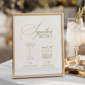 Puede incluir: Un letrero enmarcado en dorado con la frase "Signature Drinks" en escritura elegante. Debajo, ilustraciones de un espresso martini y un Old Fashioned, con sus ingredientes. El marco es dorado y el letrero est&aacute; sobre una superficie blanca.