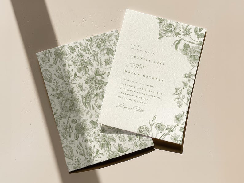 May include: A cream-coloured wedding invitation and matching envelope liner featuring a sage green botanical floral print. The invitation displays the text Victoria Rose and Mason Mathers, including the date Saturday, April 15th, 2023.