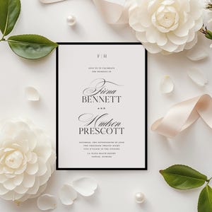 May include: A wedding invitation with a black border, featuring the names "Fiona Bennett" and "Hudson Prescott" in elegant script. The invitation is surrounded by white flowers, petals, a pearl, and a cream-coloured ribbon, creating a romantic aesthetic.