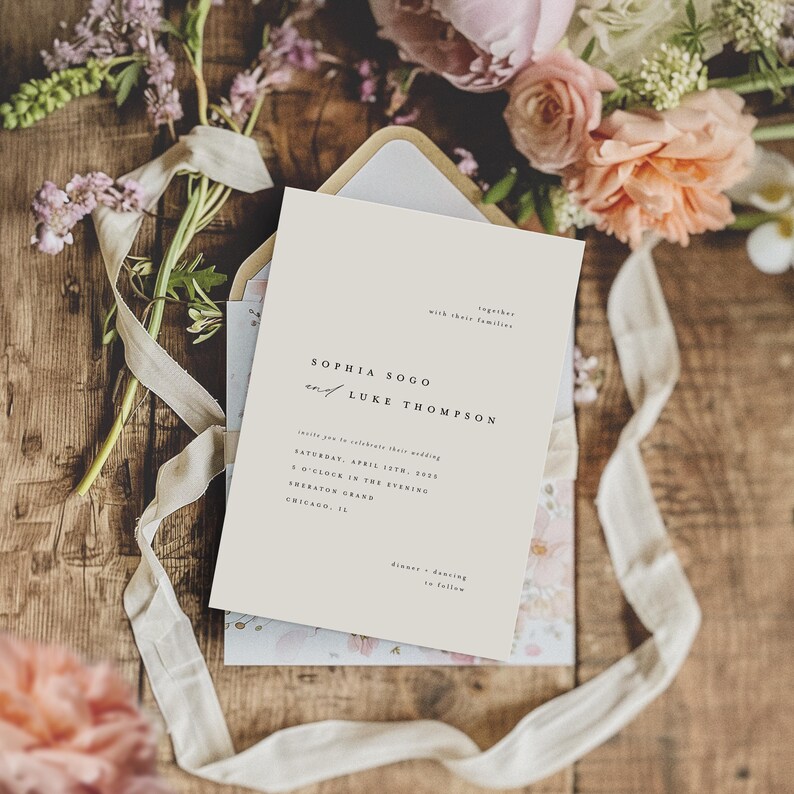 May include: A wedding invitation card with a cream background and black text. The invitation reads "Sophia Sogo and Luke Thompson" and includes the wedding date, time, and location. The card is surrounded by pink and white flowers and a white ribbon.