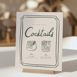 May include: A white sign with a green border and the text "Signature Cocktails" in a decorative font. The sign features illustrations of two cocktails, a Paloma and an Old Fashioned, with their ingredients listed below.