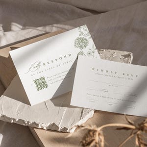 May include: Two white rectangular RSVP cards with sage green botanical illustrations. The cards feature the text KINDLY RESPOND BY THE FIRST OF APRIL, a QR code, and lines for guest names and meal selections including steak, fish, and vegetarian options.