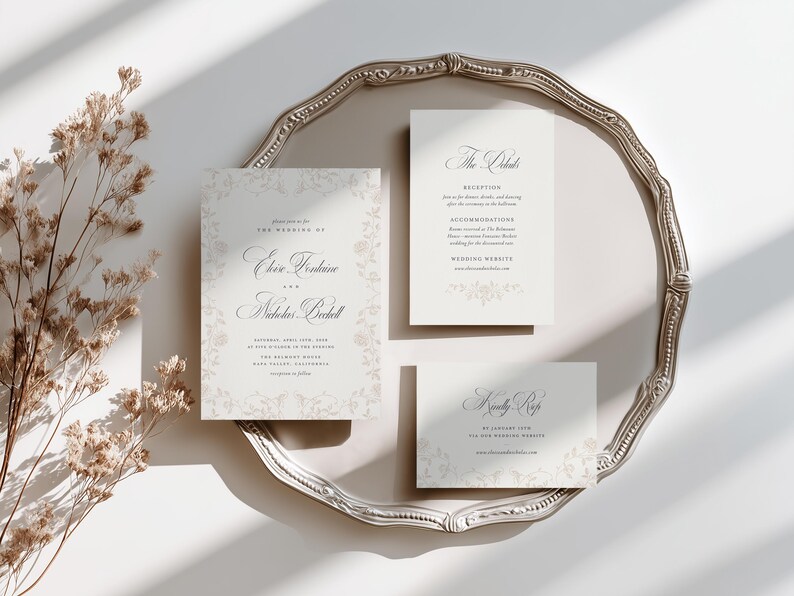May include: A set of three white wedding stationery cards with elegant black serif and script typography, featuring a faint floral border design. The cards include an invitation, a details card, and an RSVP card, all displayed on a silver tray.
