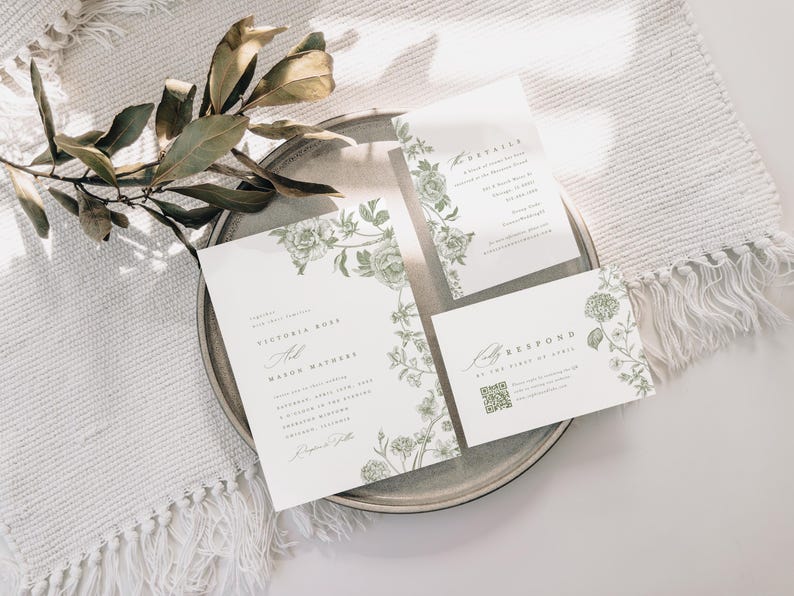 May include: A wedding invitation suite featuring three white cards with sage green botanical illustrations of roses and leaves. The text includes names Victoria Ross and Mason Mathews, event details, and a QR code on the response card.