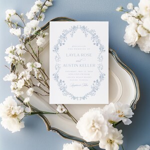 May include: A light blue wedding invitation with a floral wreath border. The invitation reads "Please join us for the wedding of Layla Rose and Austin Keller, Saturday, May 18, 20xx at five o'clock in the evening,  Captiva Beach Resort, Naples, Florida."