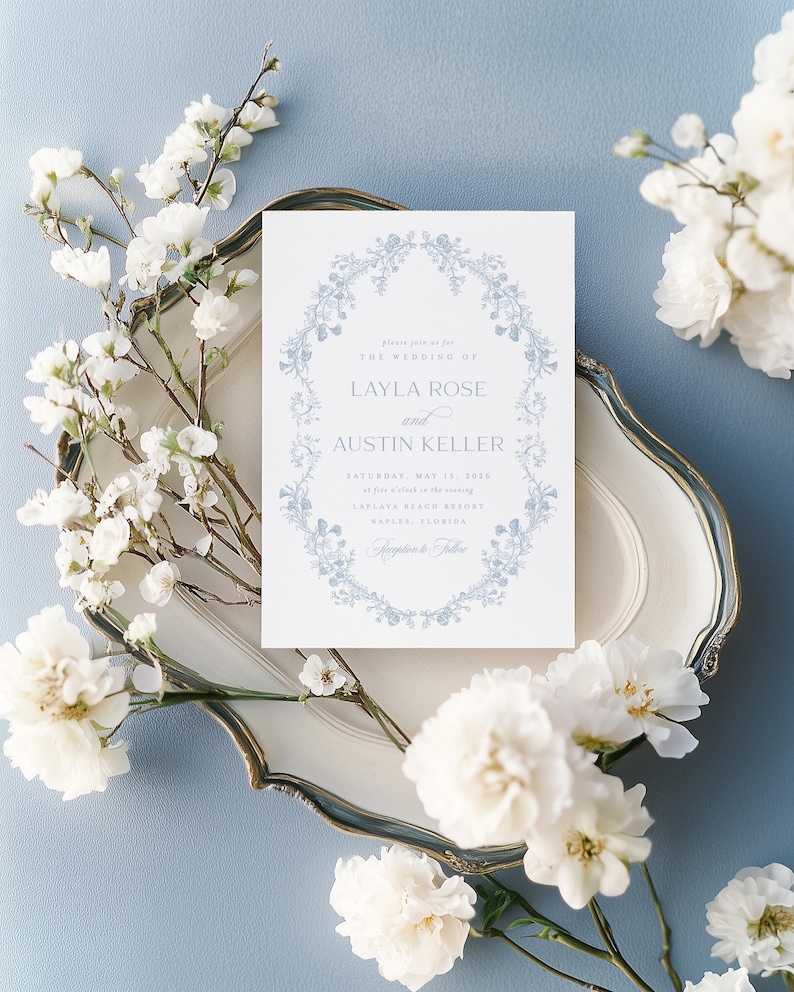 May include: A light blue wedding invitation with a floral wreath border. The invitation reads "Please join us for the wedding of Layla Rose and Austin Keller, Saturday, May 18, 20xx at five o'clock in the evening,  Captiva Beach Resort, Naples, Florida."