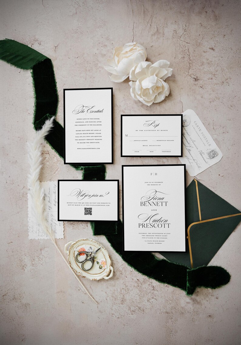 May include: A wedding stationery suite with white cards and black borders, featuring elegant calligraphy. The set includes an invitation, RSVP card, and details card. Complemented by a dark green velvet ribbon, white flowers, and a decorative tray.