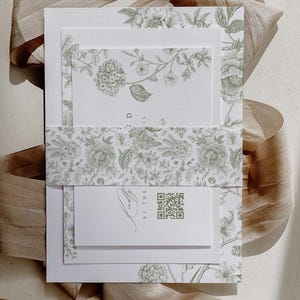 May include: A set of wedding invitations with a floral design in shades of green. The invitations are layered, with a belly band and a small card featuring a QR code. A ribbon is draped in the background.