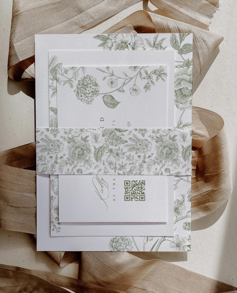 May include: A set of wedding invitations with a floral design in shades of green. The invitations are layered, with a belly band and a small card featuring a QR code. A ribbon is draped in the background.