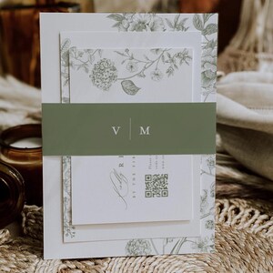 May include: A layered invitation suite featuring a floral design in shades of green and white. The suite includes a belly band with the initials "V M". The invitation has a QR code and text. The overall theme is elegant and botanical.