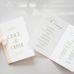 Pode incluir: Papelaria de casamento com um programa e um livreto. O livreto &eacute; amarrado com uma fita creme. O programa aberto mostra os detalhes da cerim&ocirc;nia e da festa. O texto inclui os nomes "Grace & Oliver" e a data.