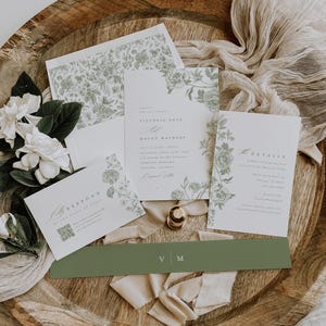 May include: A wedding invitation suite featuring white paper cards with sage green floral illustrations. The set includes a main invitation, a details card, a response card with a QR code, and a solid sage green belly band with the initials V M.