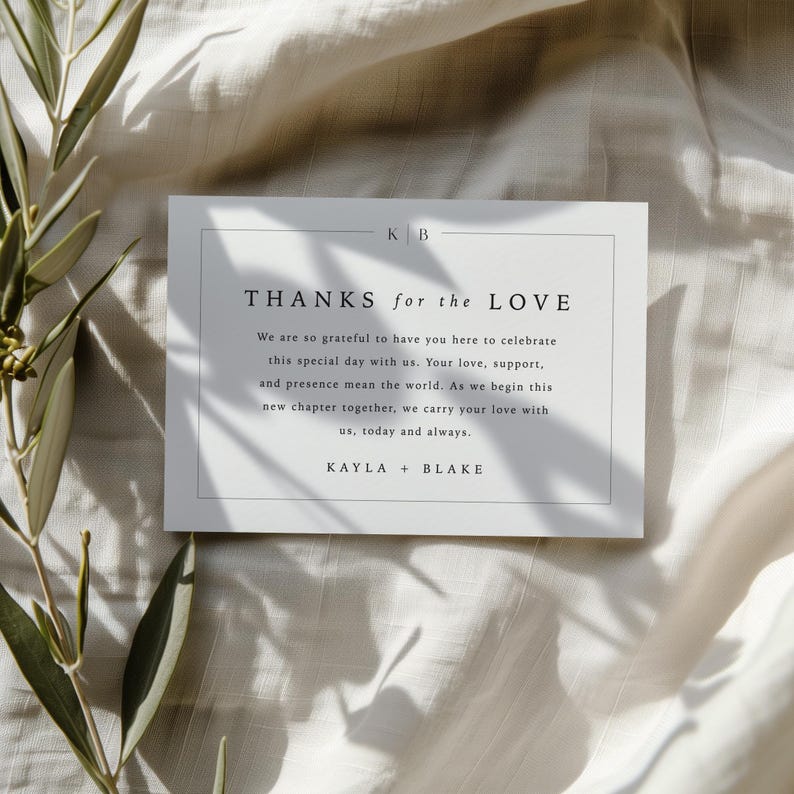 May include: A white card with the text "THANKS for the LOVE" in a minimalist font. The card includes a message of gratitude and the names Kayla + Blake. The card is on a neutral-toned fabric.