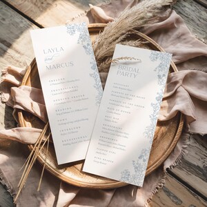 May include: Two tall, rectangular wedding program cards with white backgrounds and blue floral illustrations along the edges. The left card displays the names Layla and Marcus with a ceremony order, while the right card lists the bridal party members.