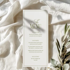 Può includere: Un menu formale con sfondo bianco e bordo verde. Il testo "The MENU" è in alto, seguito dalle opzioni di antipasto, portata principale e dessert. Il menu è decorato con rami di ulivo.