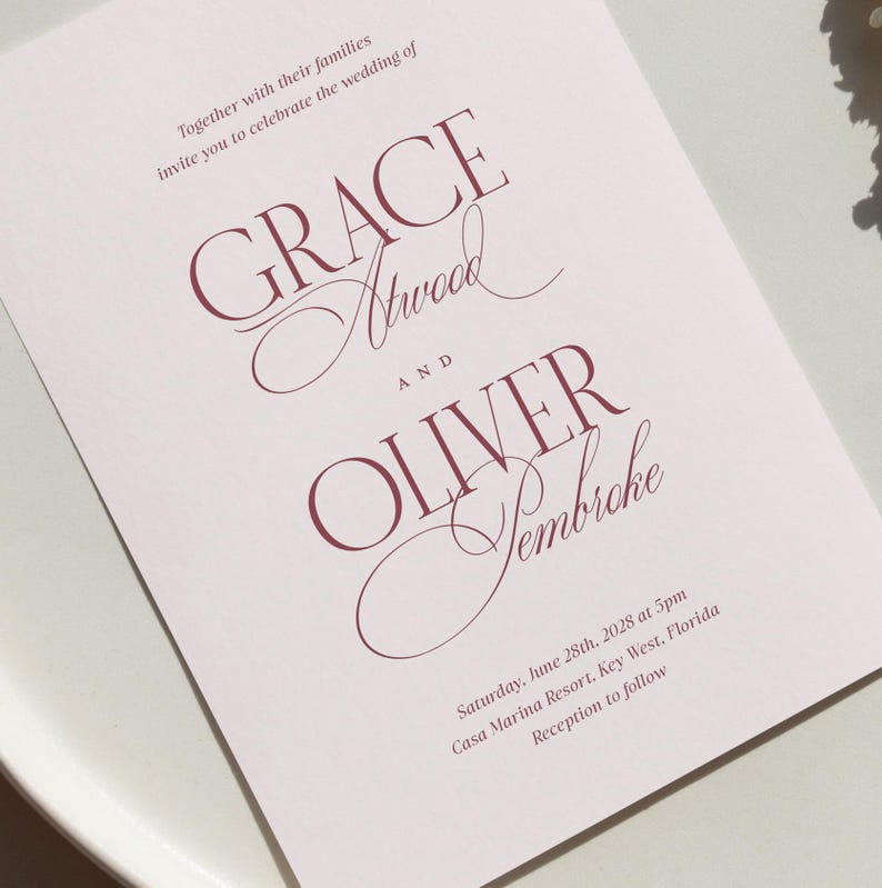 Puede incluir: Una invitaci&oacute;n de boda rosa claro con texto burdeos. La invitaci&oacute;n presenta los nombres "GRACE Atwood" y "OLIVER Yembreche". El texto tambi&eacute;n incluye la fecha, hora y lugar de la boda: Casa Marina Resort, Key West, Florida.