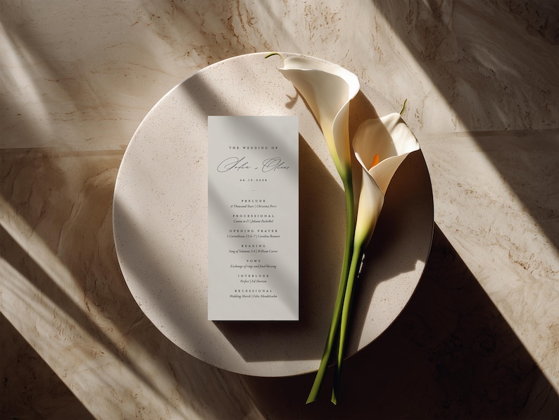 以下が含まれることがあります： The Wedding of John & Olive, 06.15.2024, Prelude, Processional, Opening Prayer, Reading, Vows, Interlude, Recessionalと黒いセリフ体および筆記体で書かれた縦型の白い結婚式プログラムカード。2本の白いカラーリリーが添えられています。