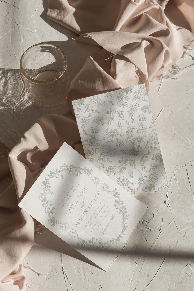 Op de afbeelding: Een huwelijksuitnodiging met een bloemmotief aan de rand en de tekst "Layla Rose en Austin Keller" in een delicaat handschrift. De uitnodiging is gedrukt op wit papier en heeft een subtiel groen bloemenpatroon.