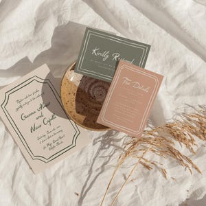 May include: Three wedding invitation cards with a green, pink, and beige color scheme. The cards are on a white linen background with a dried grass stem. The text on the cards reads "Kindly Respond", "The Details", and "Together with our families, we kindly invite you to celebrate..."