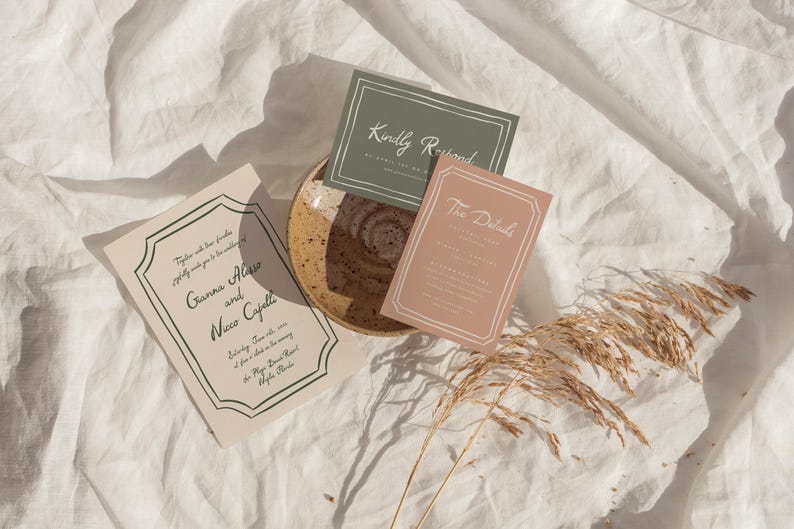 May include: Three wedding invitation cards with a green, pink, and beige color scheme. The cards are on a white linen background with a dried grass stem. The text on the cards reads "Kindly Respond", "The Details", and "Together with our families, we kindly invite you to celebrate..."