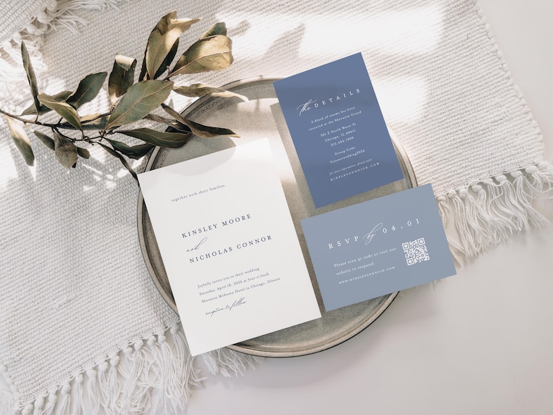 Op de afbeelding: Een huwelijksuitnodigingsset met een witte achtergrond en blauwe accenten. De uitnodigingskaart bevat de namen "Kinsley Moore" en "Nicholas Connor" in een eenvoudig, elegant lettertype. De RSVP-kaart bevat een QR-code waarmee gasten online kunnen reageren.