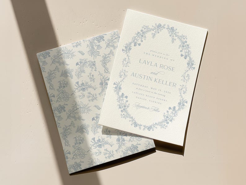 May include: A wedding invitation with a floral wreath design in blue on a white background. The invitation reads "Please join us for the wedding of Layla Rose and Austin Keller Saturday, May 13, 2023 at five o'clock in the evening Empire Place Brewery Naples, Florida Reception to follow"