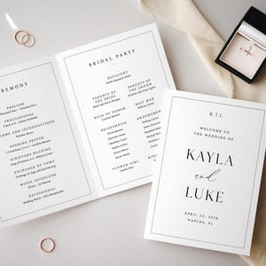 Op de afbeelding: Bruiloft briefpapier set met een drievoudig gevouwen programma, een welkomstbord en een ringdoosje. Het programma geeft de ceremonie details. Het welkomstbord toont de namen van het paar en de trouwdatum. Gouden ringen zijn ook zichtbaar.