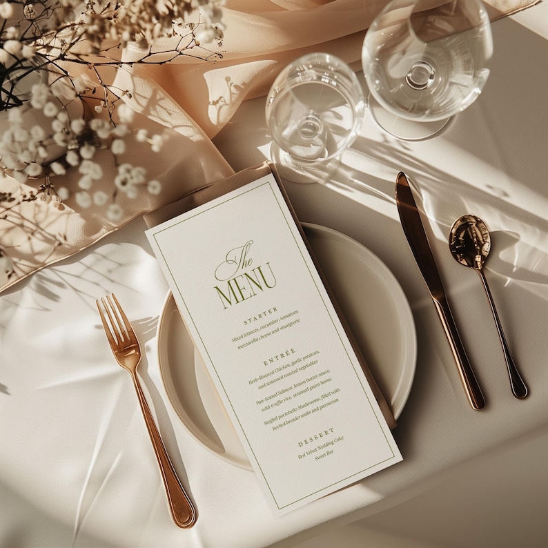 Pode incluir: Mesa elegante com um cart&atilde;o de menu, prato e talheres dourados. O cart&atilde;o de menu apresenta "The MENU" em uma fonte decorativa. Duas ta&ccedil;as de vinho e um arranjo floral contribuem para o ambiente sofisticado. Sobre uma toalha de mesa branca.