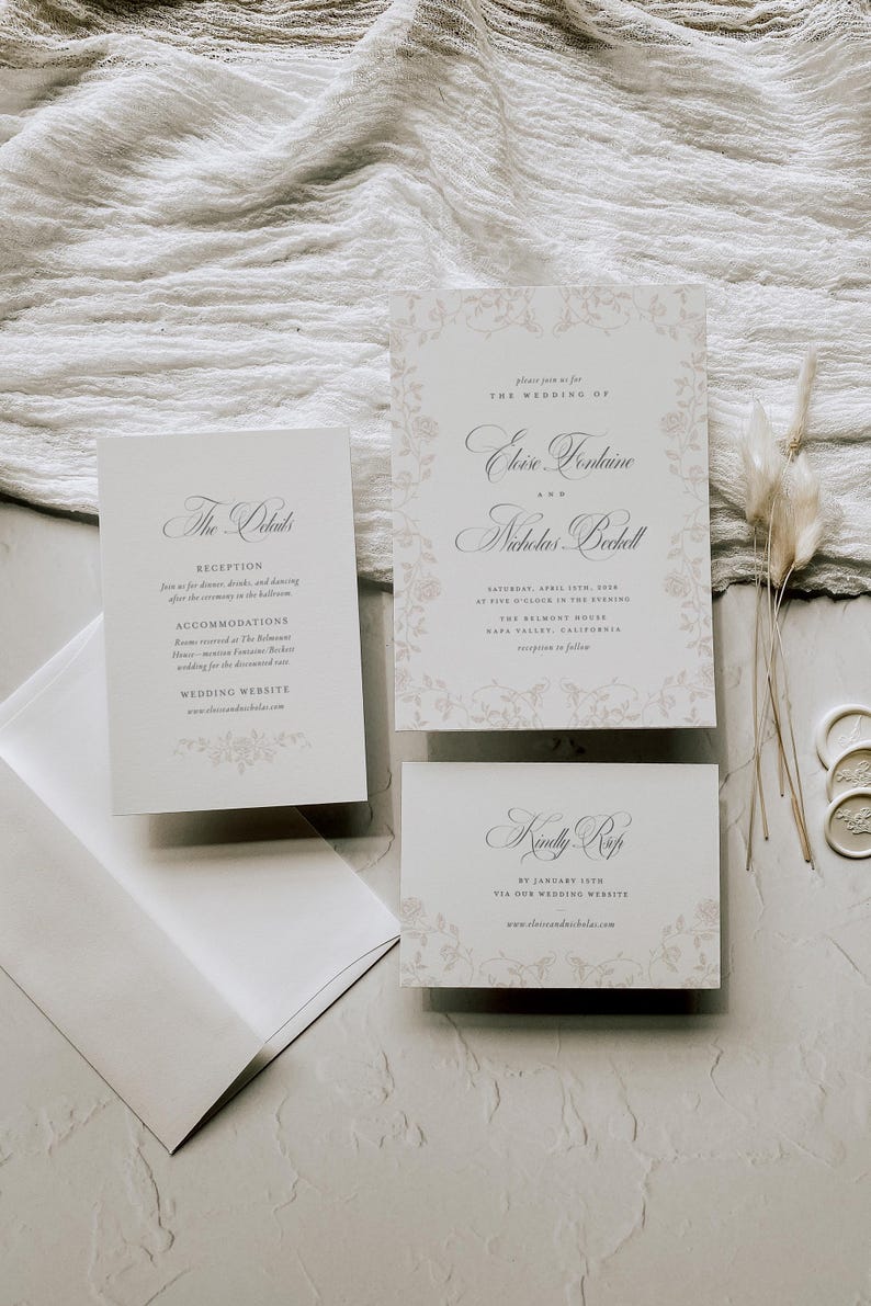 May include: A wedding invitation suite featuring a main invitation, a details card, and an RSVP card, all printed on white cardstock with light beige floral borders and elegant black serif and script typography, accompanied by a white envelope.