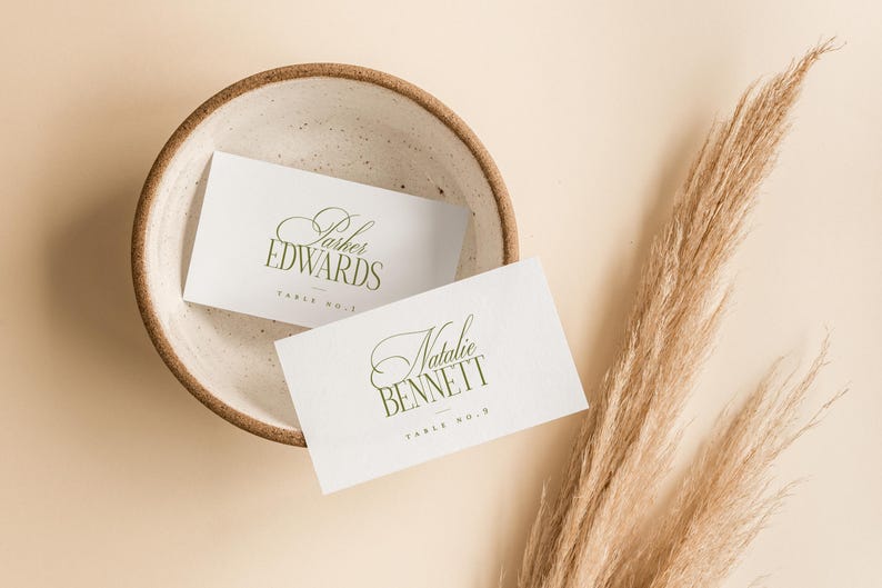 Pode incluir: Dois cart&otilde;es de mesa brancos com letras verdes elegantes, um com a inscri&ccedil;&atilde;o "Parker Edwards" e o outro com "Natalie Bennett". Eles est&atilde;o em uma tigela de cer&acirc;mica salpicada. A grama pampas seca adiciona um toque natural.