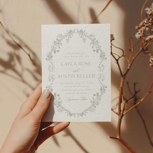 Op de afbeelding: Een witte huwelijksuitnodiging met een bloemige rand en de tekst "U wordt uitgenodigd voor de bruiloft van Layla Rose en Austin Keller Zaterdag 17 mei 2018 om 16:00 uur Chapel Bells Ranch Waco, Texas"