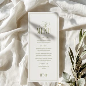 May include: A formal menu card with a white background and a thin, double border. The text "The MENU" is in an elegant script, with the menu items in a serif font. The menu includes starters, entrees, and dessert options. The initials "H&M" are at the bottom.