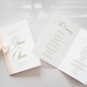 Puede incluir: Programas de boda con caligraf&iacute;a elegante. Un programa est&aacute; cerrado con una cinta crema, el otro est&aacute; abierto, mostrando los detalles de la ceremonia y la fiesta. El texto dice "Grace and Oliver" y la fecha.