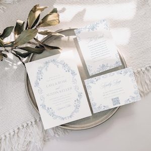May include: A set of three wedding invitations with a floral design in shades of blue. The main invitation features the names "Layla Rose" and "Austin Keller" in a script font. The other two cards are for the ceremony and reception.