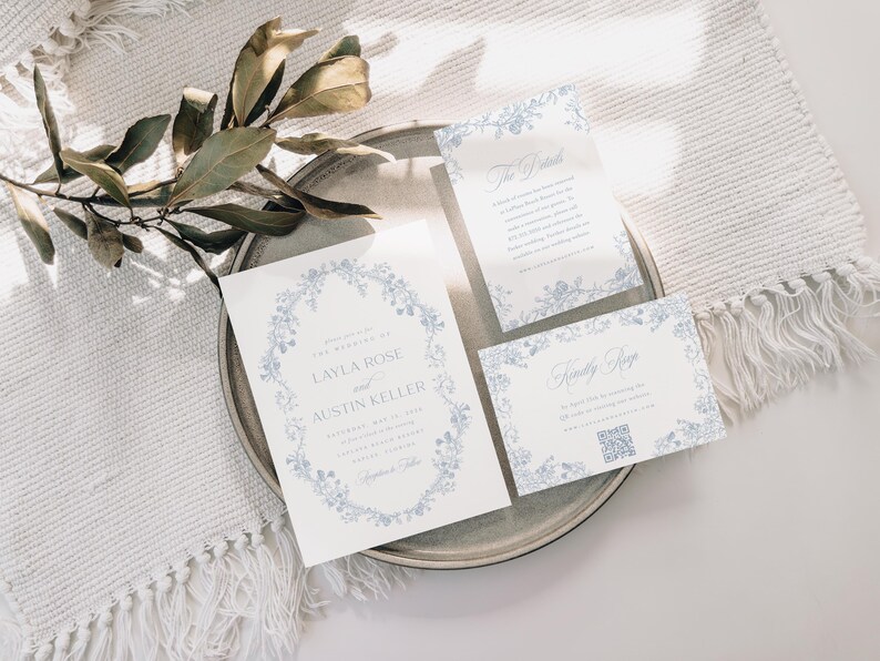 May include: A set of three wedding invitations with a floral design in shades of blue. The main invitation features the names "Layla Rose" and "Austin Keller" in a script font. The other two cards are for the ceremony and reception.