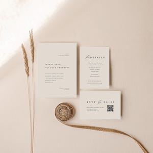 May include: A minimalist wedding invitation suite with a cream background. The invitation card features the names "Sophia Bogo and Luke Thompson" in a simple font. The details card includes the date, time, and location of the wedding. The RSVP card has a QR code for guests to respond.
