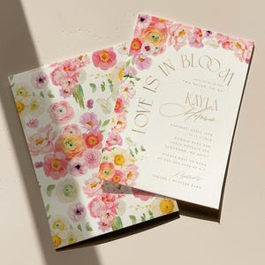 May include: Two floral wedding invitations with a watercolour design. The invitations feature pink, yellow, and peach flowers with green leaves. One invitation reads "Love is in Bloom" and includes event details.