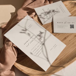 May include: A wedding invitation with a minimalist design featuring the names Sophia Sogo and Luke Thompson, the date Saturday, April 15th, 2023, and the time 5 o'clock in the evening. The invitation is printed on a cream-colored card with a shadow of a branch behind the text.