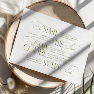Pode incluir: Um cart&atilde;o de menu de casamento com uma elegante escrita verde-oliva, listando pratos como "Come&ccedil;o", "Prato principal" e "Final doce". O cart&atilde;o repousa sobre um prato bege, com um tecido branco e sombras no fundo.