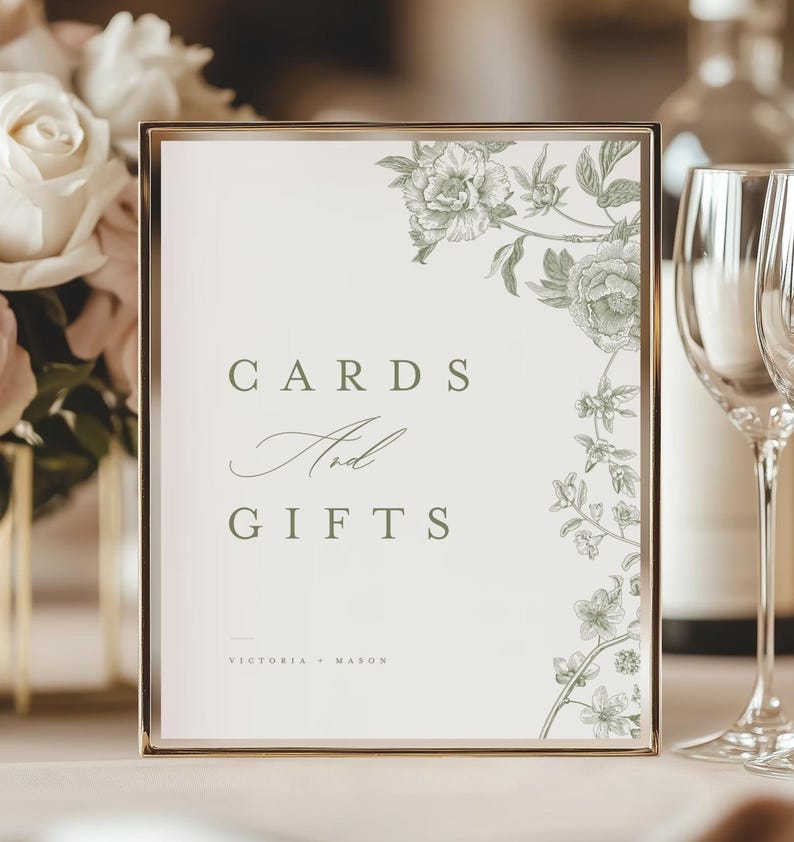 May include: A framed sign with the words "CARDS And GIFTS" in a serif font. The sign has a gold frame and a floral design in the upper right corner. The names "VICTORIA + MASON" are printed at the bottom of the sign.