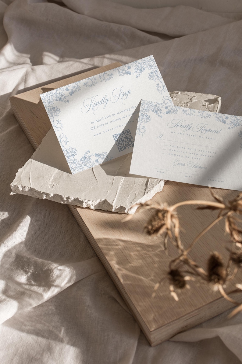 May include: Two white cards with blue floral borders and text. The top card says "Kindly RSVP by April 15th by scanning the QR code or visiting our website." The bottom card says "Kindly Respond by the 15th of April."