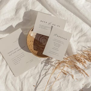 May include: A set of three minimalist wedding invitation cards with a simple design. The cards are printed on a cream-colored paper and feature a handwritten font. The text on the cards includes the names "Sophia Good" and "Luke Thomas", the date "04-01", and the words "RSVP" and "Details".