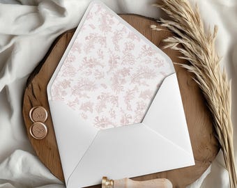 May include: A white envelope with a floral patterned interior, displayed on a wooden surface. The envelope is open, revealing a delicate pink floral design. Two gold wax seals and a wooden handled wax stamp are also present.