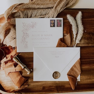 May include: Two white envelopes with floral designs and text, one sealed with a gold wax stamp. The envelopes are on a wooden surface with fabric and dried flowers. One envelope has stamps.