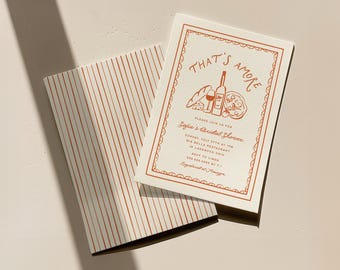 May include: A white invitation with a red border and text that says "That's Amore" with a graphic of a bottle of wine, a glass of wine, bread, cheese, and a pizza slice. The text also says "Please join us for Sofia's Bridal Shower" and includes the date, time, location, and RSVP information.