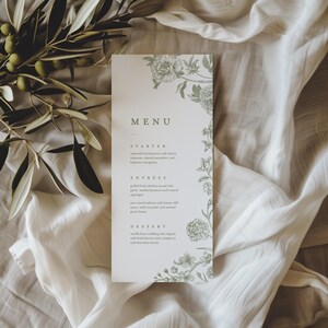 May include: A vertical rectangular menu card printed on white paper with sage green botanical illustrations of flowers along the right edge. The text includes the headings Menu, Starter, Entrees, and Dessert with detailed food descriptions.