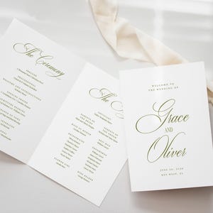Puede incluir: Programas de boda blancos con letras verdes. Los programas abiertos muestran los detalles de la ceremonia, y un programa cerrado muestra los nombres "Grace y Oliver". Una cinta color crema est&aacute; cerca.