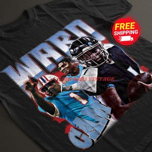 May include: Black t-shirt with a graphic print of three football players. The players are wearing blue and white uniforms. The text "WARD" and "GAY" are printed on the shirt.