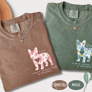 May include: Two Comfort Colors t-shirts, one espresso and one moss green, each featuring a floral French bulldog graphic. The shirts have the text "Life's better with a Frenchie" and a small pendant necklace. The espresso shirt says "Luna".