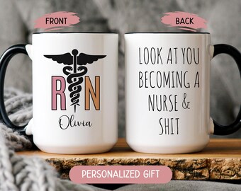 May include: White ceramic mug with black handle and rim. The front features a medical symbol, the letters "RN" in pink and orange, and the name "Olivia". The back of the mug says "LOOK AT YOU BECOMING A NURSE & SHIT".